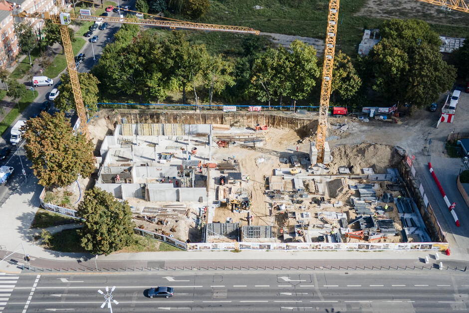 zdjęcie z drona, widać plac budowy, betonowe elementy i dwa duże żurawie budowlane