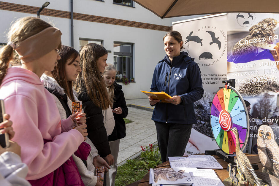 Kobieta mówi do dzieci na stoisku edukacyjnym w ogrodzie przed budynkiem.