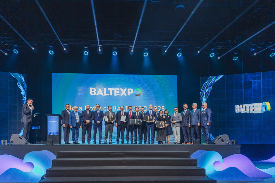 Grupa osób stoi z nagrodami na scenie.