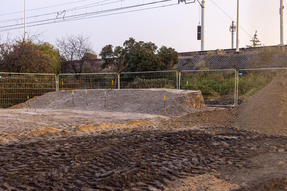 na zdjęciu uformowany ziemny wał, widać plac budowy, gruntowy, otoczony ogrodzeniem
