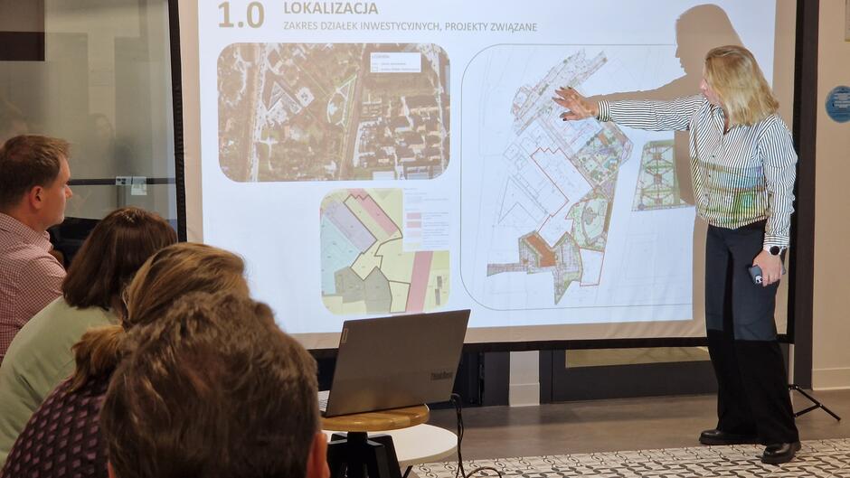 Kobieta przy planszy pokazuje teren na wyświetlanej prezentacji