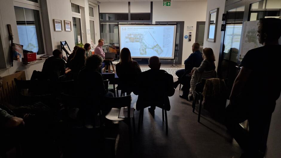 Ciemne sylwetki ludzi na sali patrzących na wyświetlaną prezentację