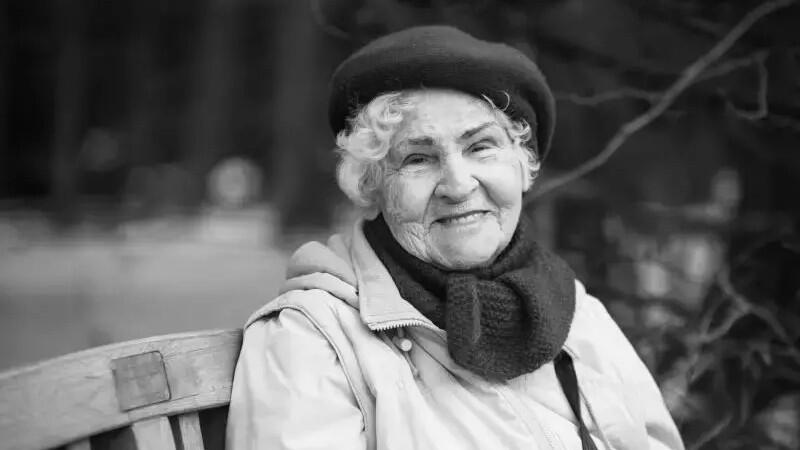 Czarno-białe zdjęcie. Uśmiechnięta starsza pani w berecie, szalu i kurtce