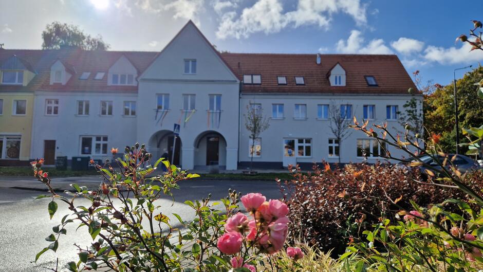 Biały budynek z arkadowym wejściem i skośnymi dachami z czerwoną dachówką,