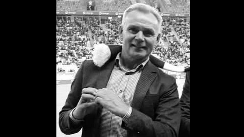 Czarno-białe zdjęcie. Uśmiechnięty mężczyzna w średnim wieku na tle trybun stadionu