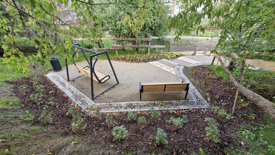 na zdjęciu dwie ławki, na uporządkowanym parkowym terenie