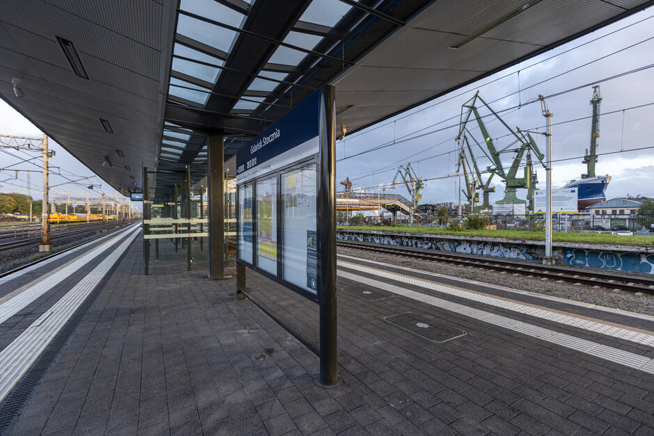 na zdjęciu nowoczesna wiata przystanku kolejowego, po prawej w tle dźwigi stoczniowe