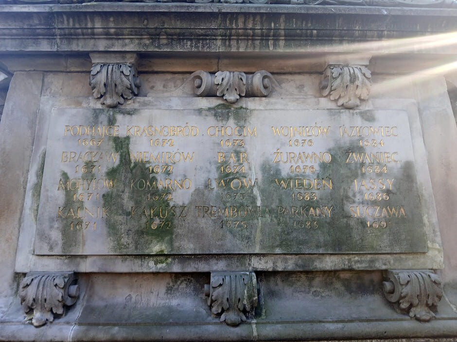 Cokół pomnika z napisami, na którym widać brud i glony.