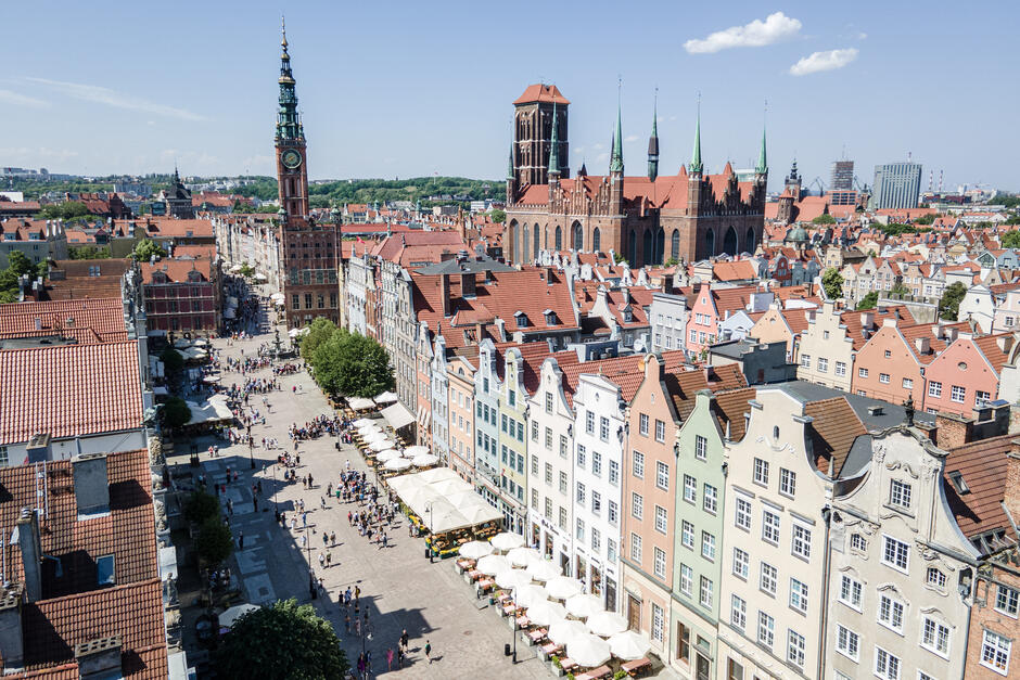 zdjęcie z drona, widać kamienice gdańskie przed nimi deptak z ludźmi, w tle ogromna bazylika mariacka
