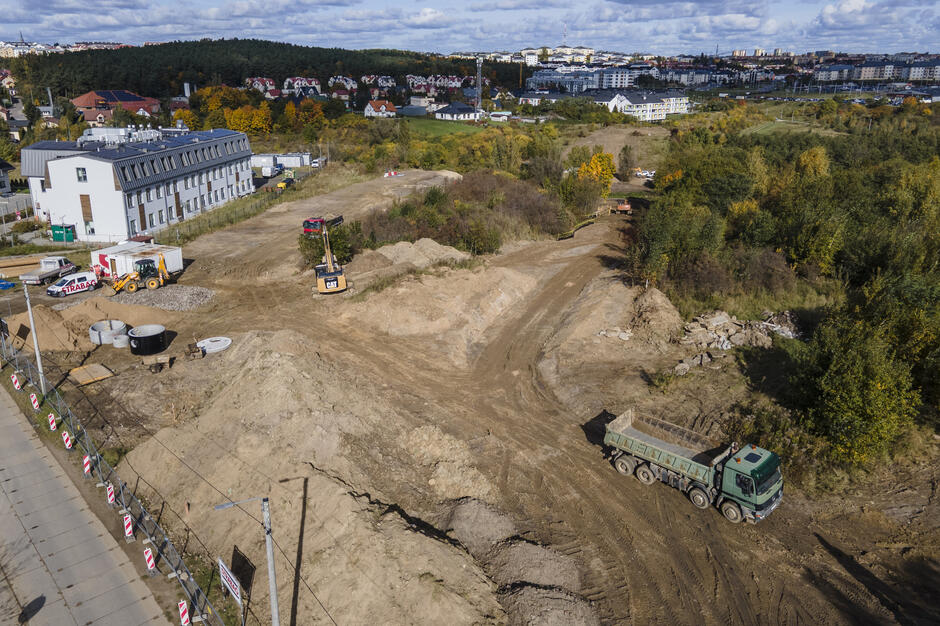 na zdjęciu plac budowy, widać rozkopany teren i koparki oraz ciężarówki