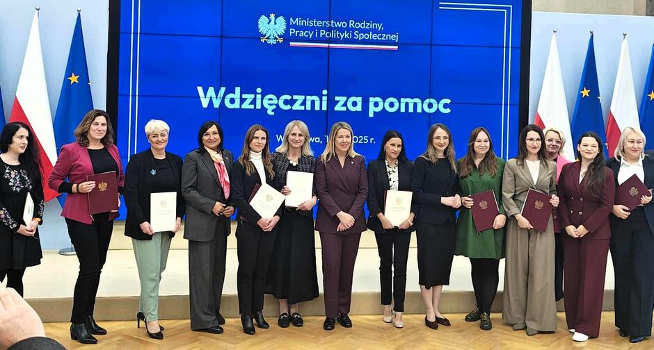 Kilkanaście osób pozuje do zdjęcia na tle ekranu z napisem Wdzięczni za pomoc .