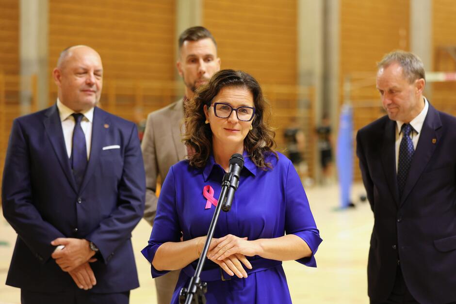 Prezydent Gdańska mówi przez mikrofon, za nią stoją trzy osoby