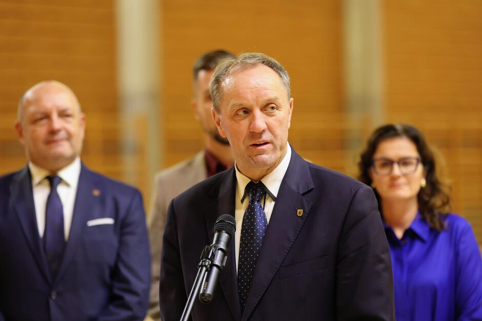 Mężczyzna po sześćdziesiątce, przemawia do mikrofonu