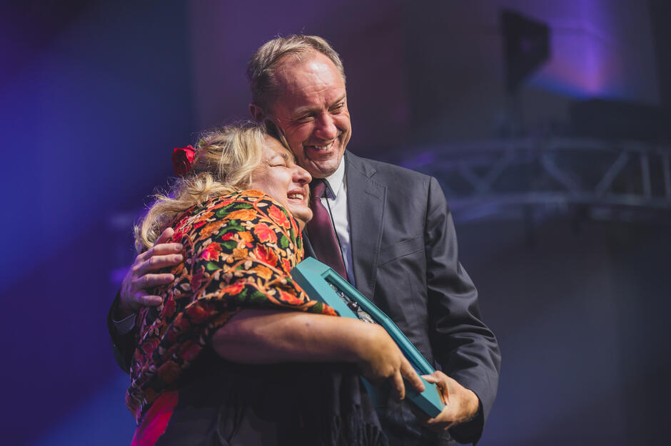 Kobieta i mężczyzna na scenie przytulają się i śmieją.