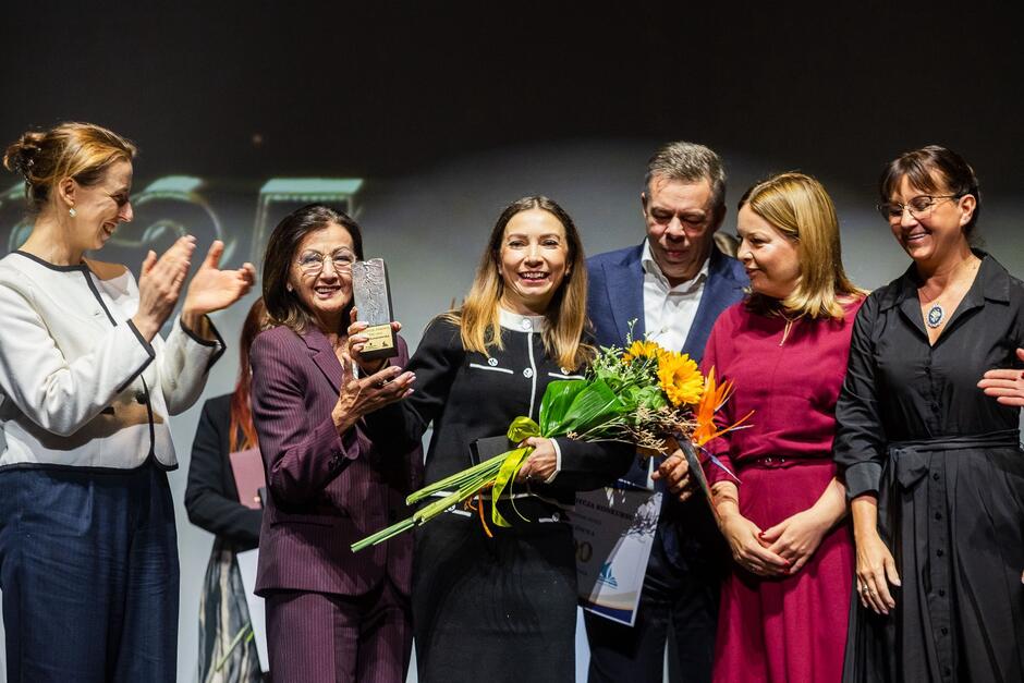 Kilka osób na scenie, stoją z laureatką