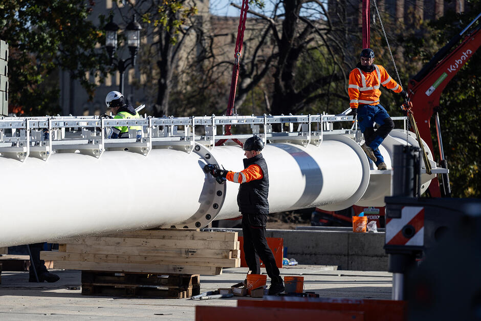 Trzech mężczyzn pracuje przy leżącym wielkim stalowym maszcie. 