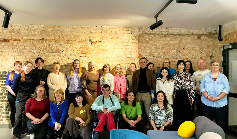 Zdjęcie przedstawia grupę osób, które stoją na tle ściany z cegieł.