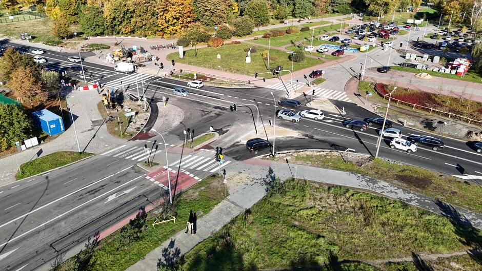 Widok z góry na skrzyżowanie, na którym prowadzone są prace drogowe i obowiązuje tymczasowa organizacja ruchu. Na jezdniach widać sznur samochodów oraz maszyny budowlane pracujące przy modernizacji nawierzchni. 
