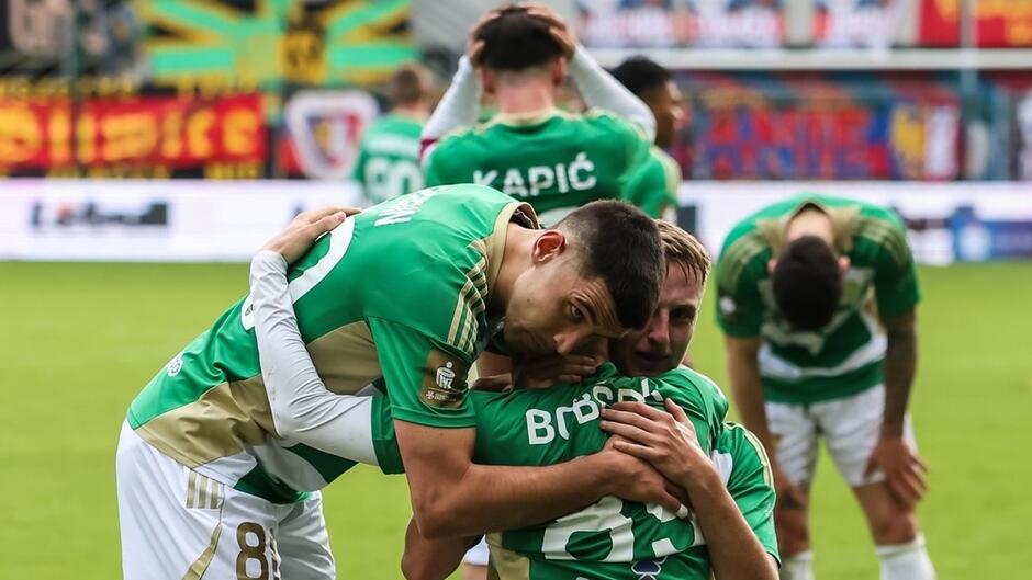 Kilku zawodników w biało zielonych strojach, podczas meczu