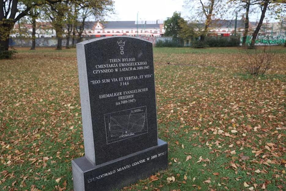 Płyta z ciemnego kamienia na terenie parkowym z napisem: Teren byłego cmentarza ewangelickiego