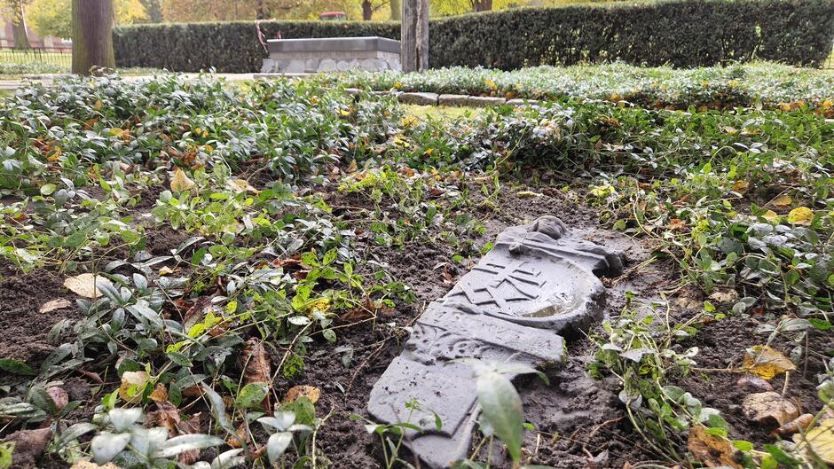 Złamany fragment rzeźbionego nagrobka ułożony na ziemi