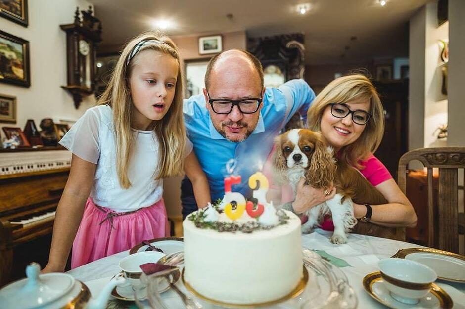 Adamowicz zdmuchuje świeczkę na torcie. Po swojej prawej stronie ma córkę, po lewej - żonę