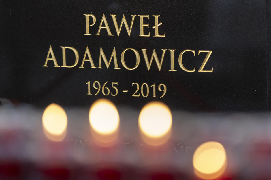 Czarna marmurowa płyta pionowo wmurowana w ścianę, ze złoconymi napisami: Paweł Adamowicz 1965 - 2019 
