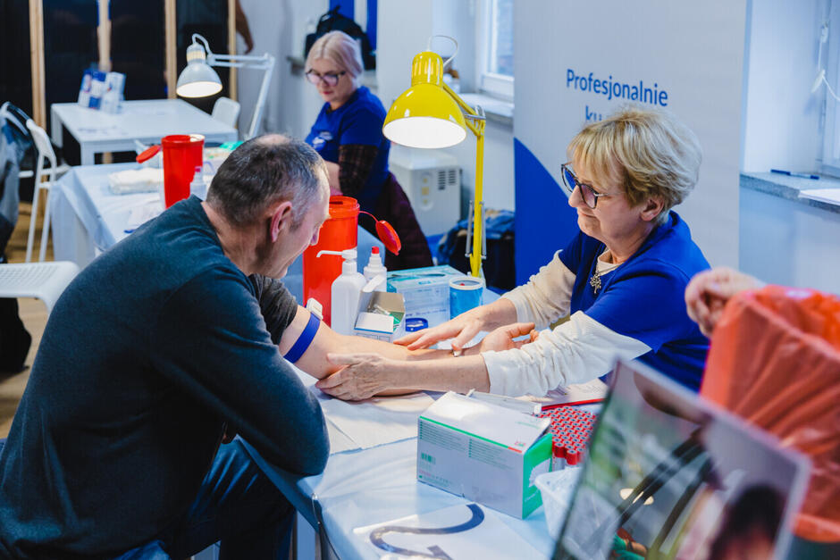 Zdjęcie przedstawia pielęgniarkę pobierającą krew od mężczyzny w strefie badań