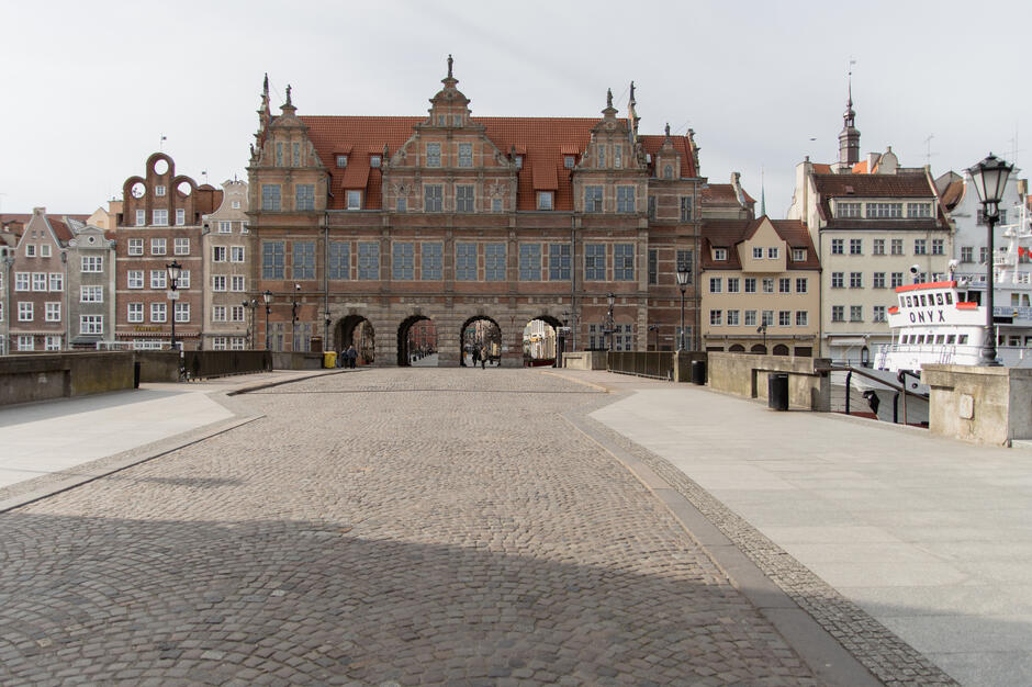 na zdjęciu na pierwszym planie brukowana ulica, w tle zabytkowa gdańska, bogato zdobiona brama wjazdowa do miasta