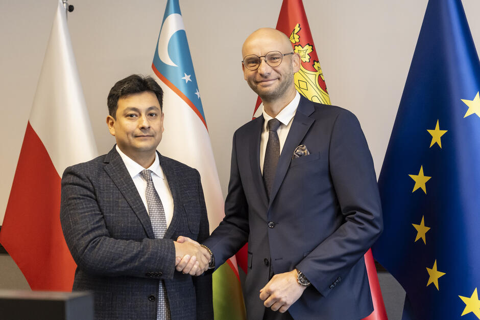 Dwaj mężczyźni stoją naprzeciwko siebie, witając się poprzez uściśnięcie ręki