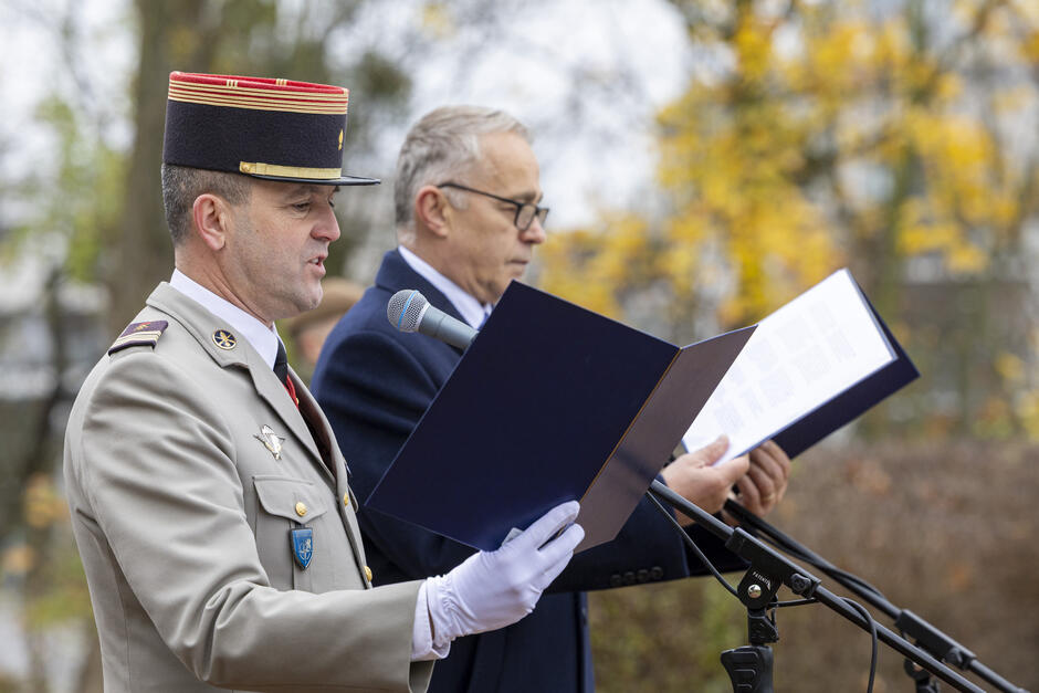 na zdjęciu francuski żołnierz w mundurze jasnym i konsul francji w ciemnym płaszczu, obaj czytają z kartek do mikrofonów