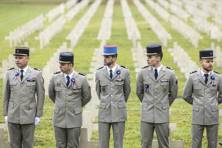 na zdjęciu pięciu żołnierzy w szarych galowych mundurach, za nimi kilka rzędów białych krzyży