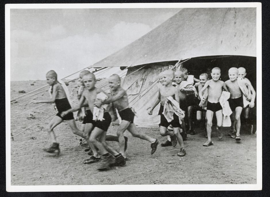 Grupa chłopców wybiegających z namiotu, są bez koszulek, zapewne panuje upał