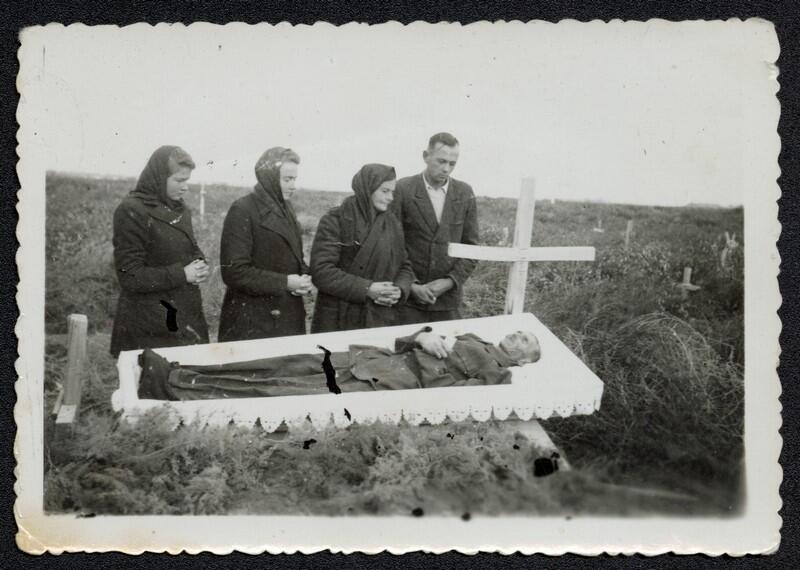 Cztery osoby nad otwartą trumną na cmentarzu - trzy kobiety i młody mężczyzna po prawej