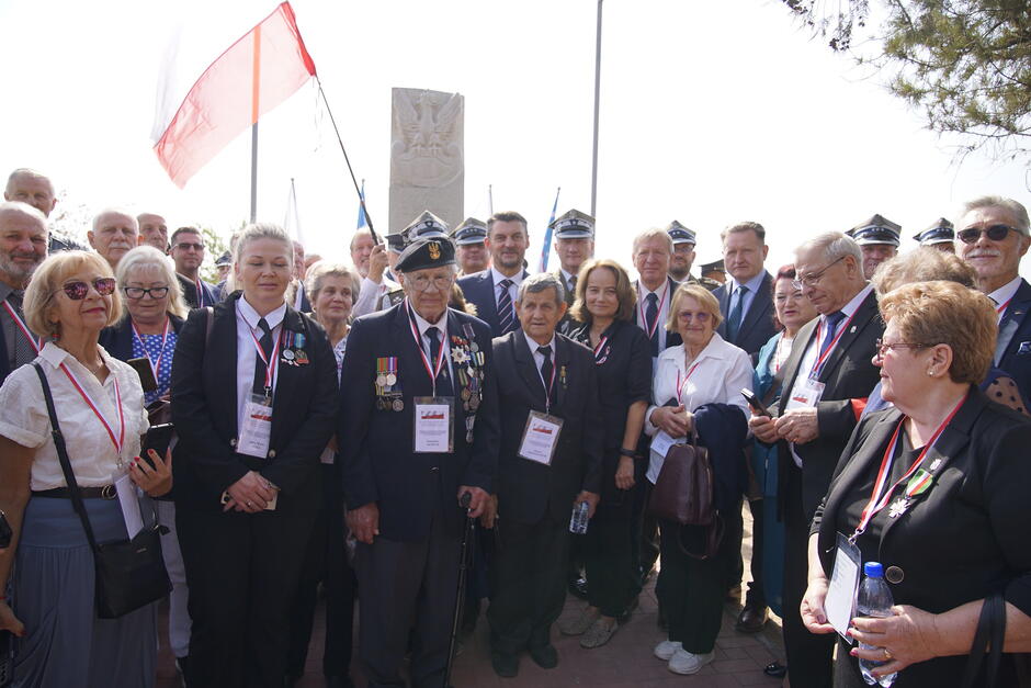 Grupa osób ustawionych do wspólnego zdjęcia z pomnikiem w tle