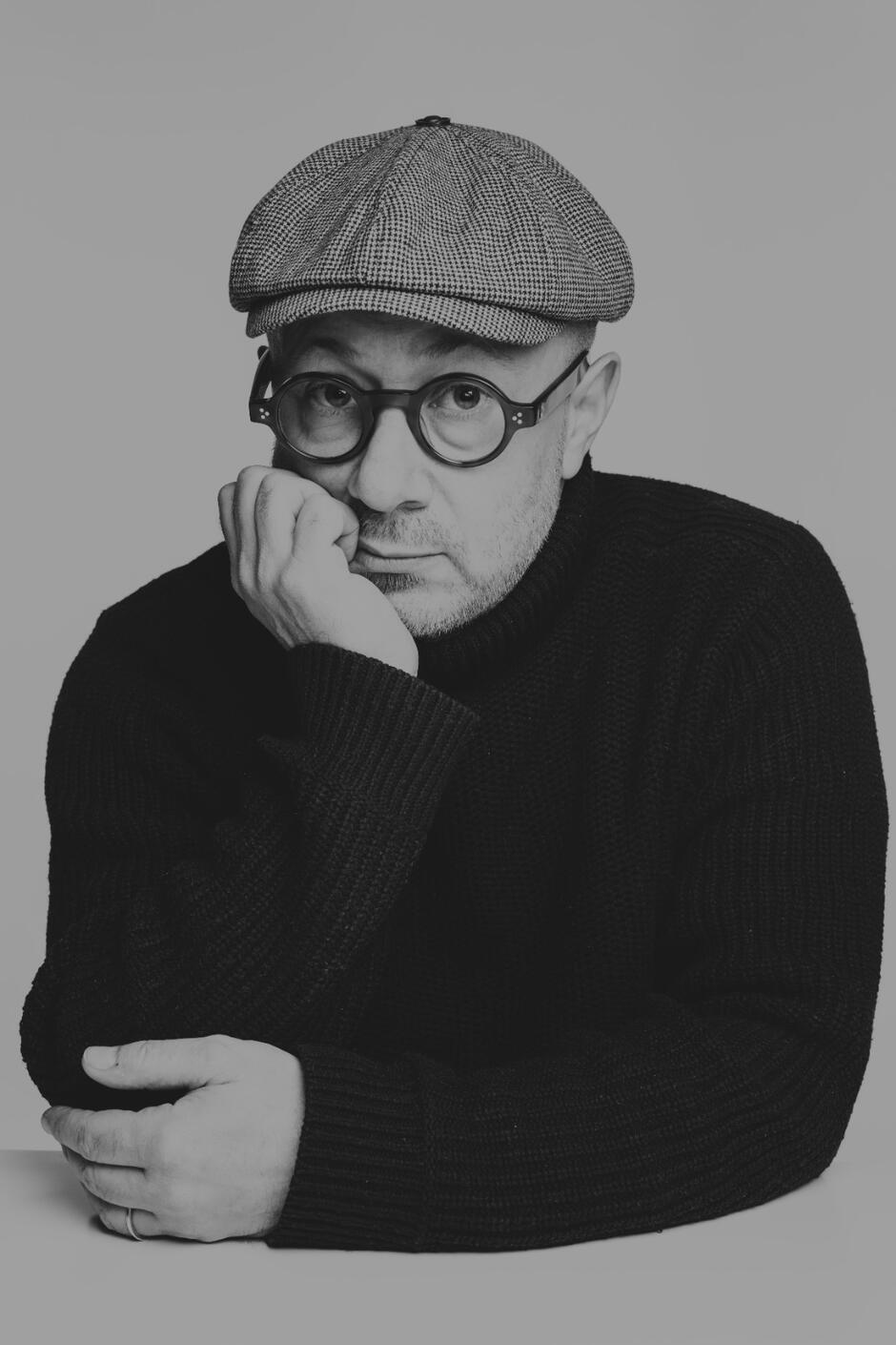 zdjęcie mężczyzny w okularach i czapce z ręką podparta na brodzie 