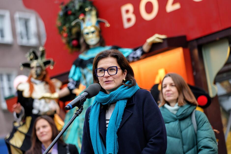 zdjęcie wręcz portretowe, widać kobietę w średnim wieku, szatynkę w okularach, mówi do mikrofonów