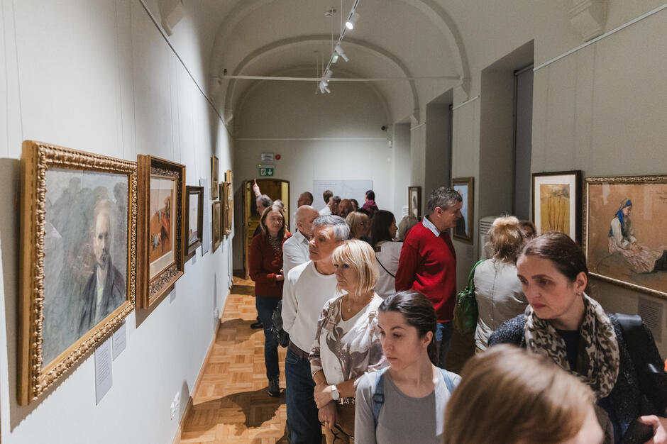 Tłum ludzi zwiedza wystawę malarstwa. 