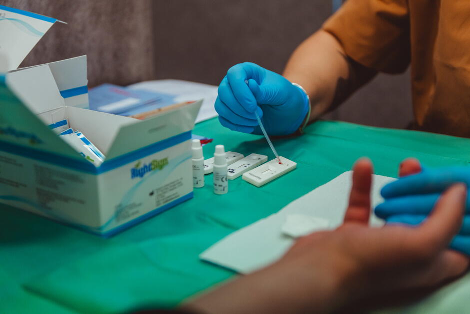 na zdjęciu medyczne plastikowe białe urządzenia do badań, widać rękę w rękawiczkach niebieskich trzymającą dłoń osoby siedzącej naprzeciwko