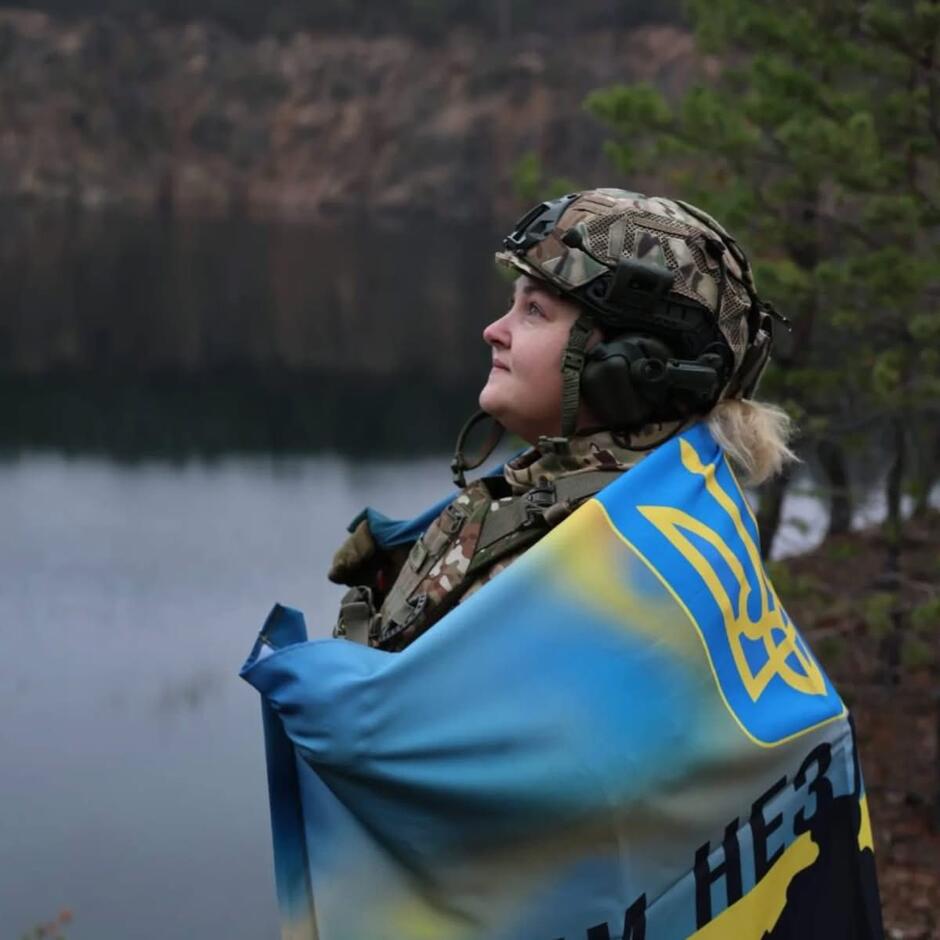 Młoda kobieta w wojskowym mundurze i hełmie, owinięta ukraińską flagą