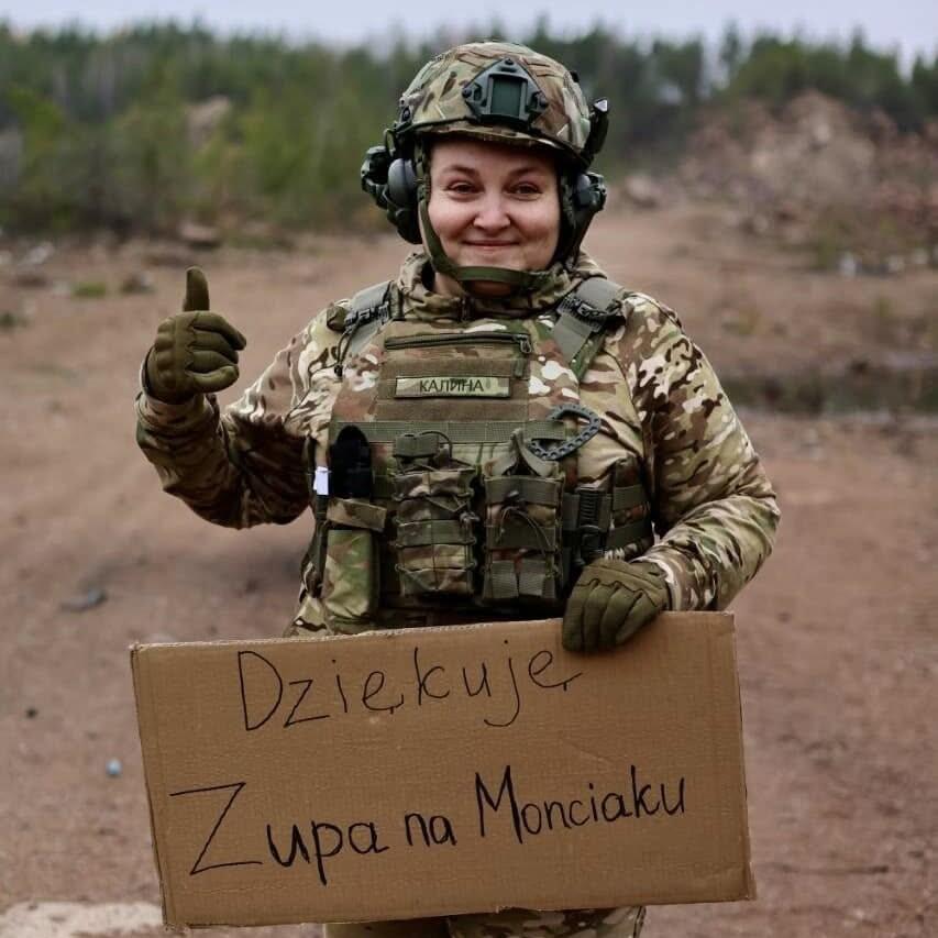 Kobieta w mundurze i hełmie, z kartonowym prostokątem w ręce, na którym jest napis Dziękuję Zupa na Monciaku!