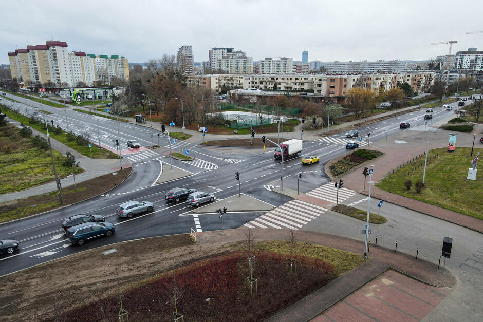 na zdjęciu skrzyżowanie ulic, jadą samochody, w tle kilka wysokich bloków mieszkalnych