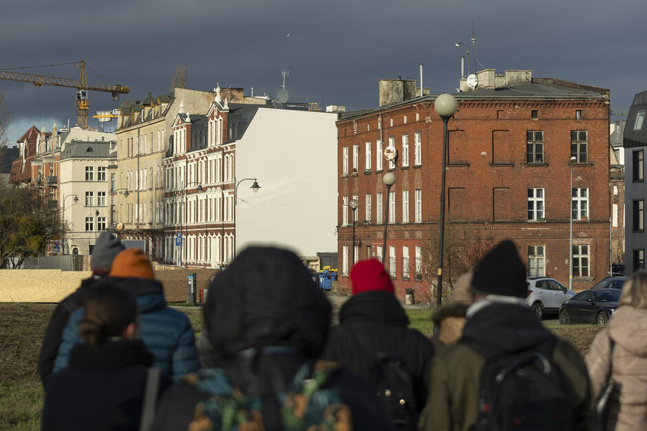 Grupa ludzi na spacerze po mieście ogląda rewitalizowaną dzielnicę.