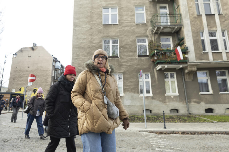 Kobieta z mikrofonem prowadzi spacer po rewitalizowanej dzielnicy miasta.