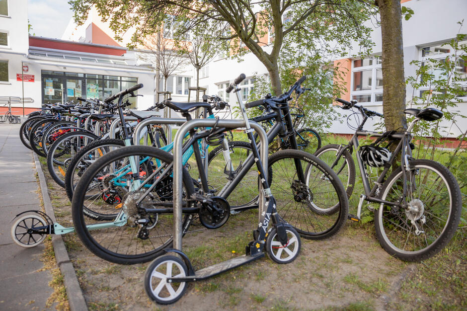 Przed budynkiem szkoły widać długi rząd zaparkowanych rowerów oraz hulajnogę przypiętą do stojaka. Uczniowie najwyraźniej licznie korzystają z ekologicznych środków transportu.
