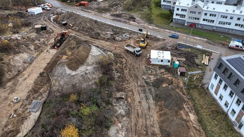 zdjęcie z drona, widać rozkopany plac budowy z ciężarówkami i koparkami