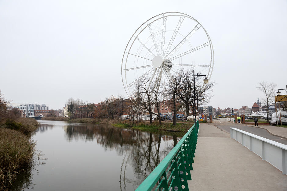 Koło widokowe widziane od strony mostu na rzece w mieście.