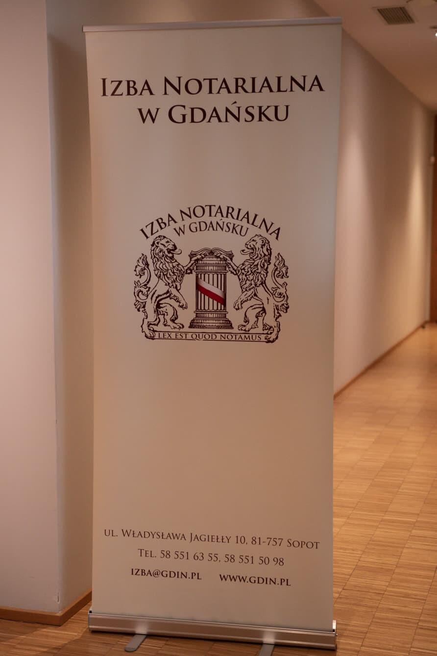 Roll-Up z nadrukowanym logo Izby Notarialnej w Gdańsku, który stoi w korytarzu prowadzącym do sali, gdzie udzielano porad