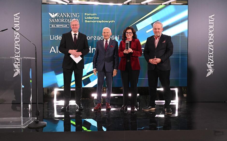 na zdjęciu trzech starszych mężczyzn i jedna kobieta, wszyscy pozują do zdjęcia, w oficjalnych eleganckich strojach