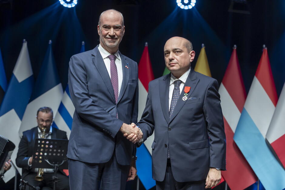 Dwaj mężczyźni pozują na scenie do zdjęcia, ten po prawej ma medal przypięty do piersi